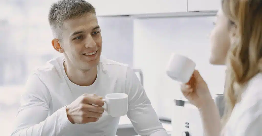 A couple drinking coffee and talking at a kitchen counter.