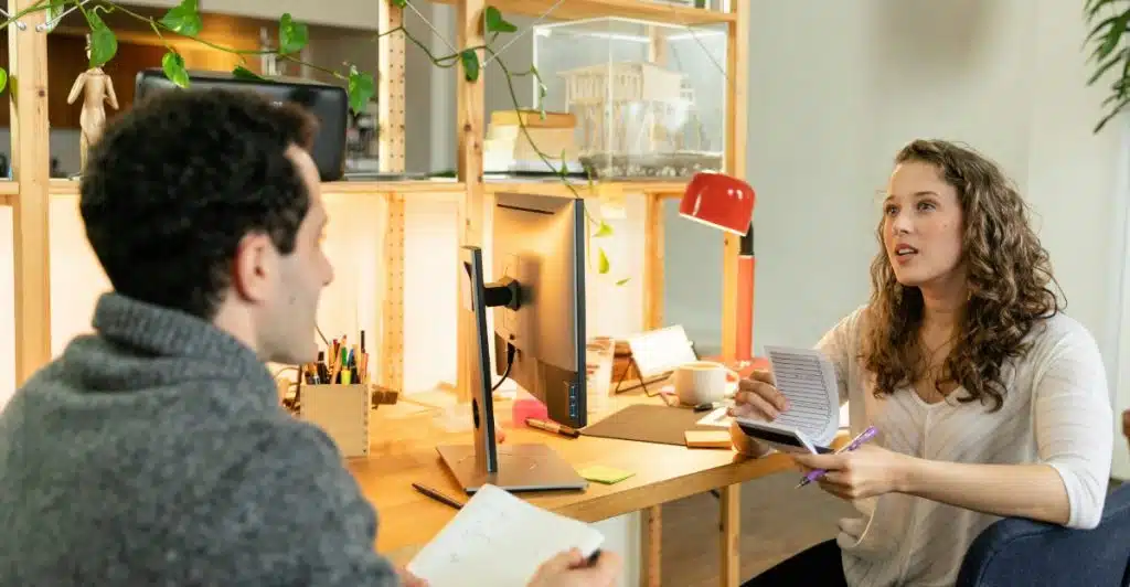 A woman talking while sitting at a desk with a man.