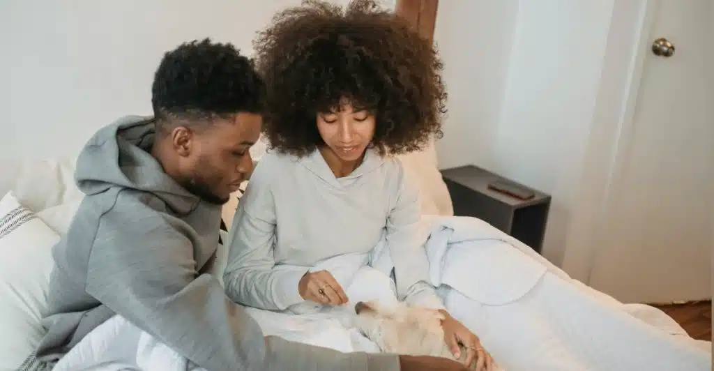 A couple petting a dog while sitting in bed.