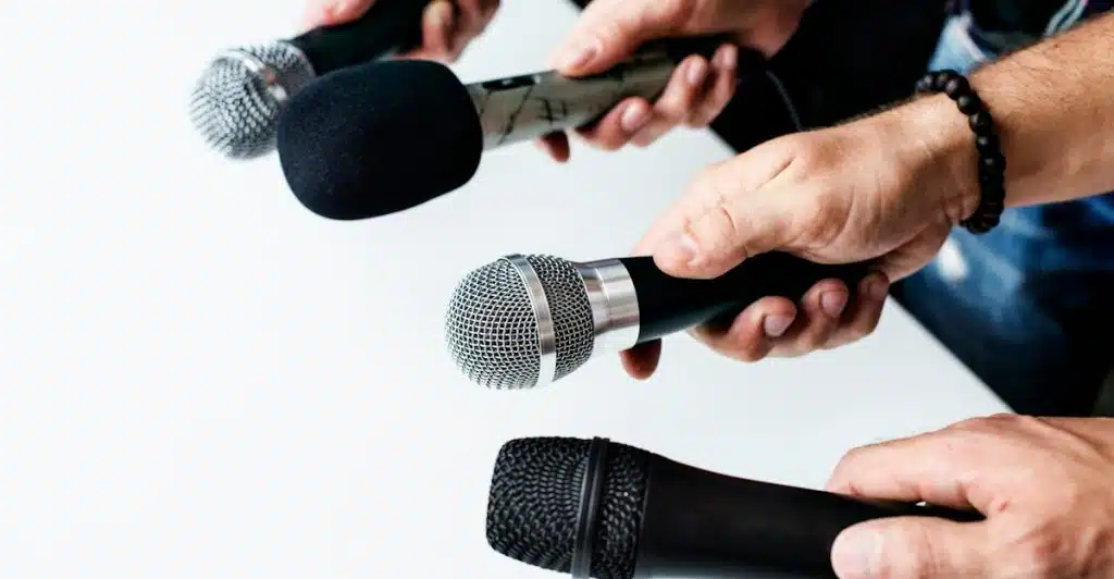 Several hands holding different microphones.