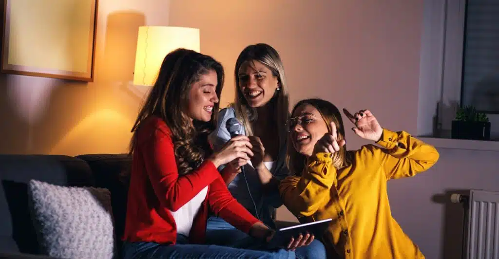 Three women cheerfully singing karaoke on a couch.