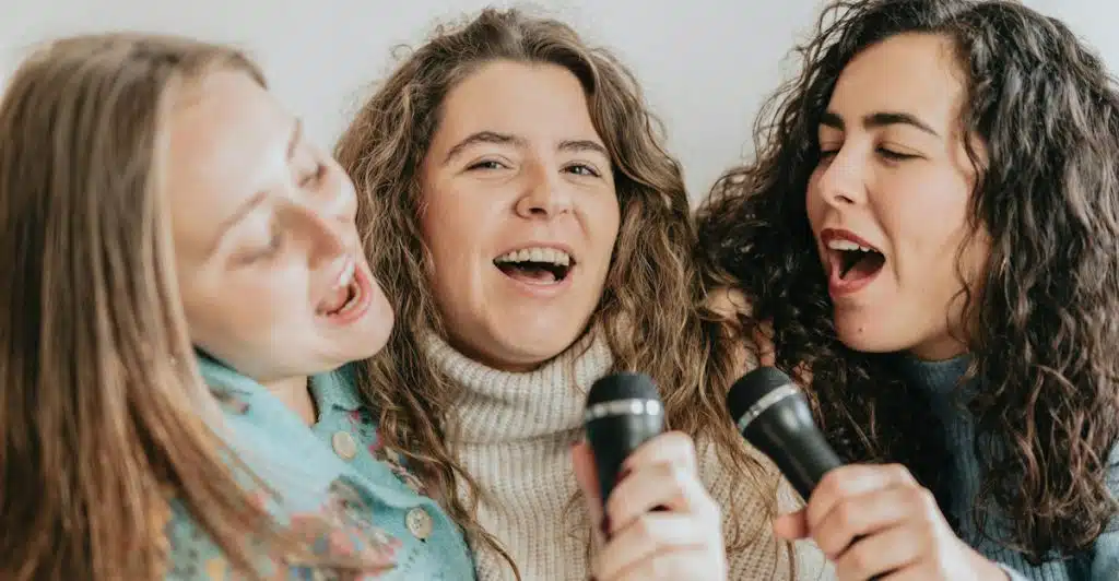 Three women singing into microphones together.