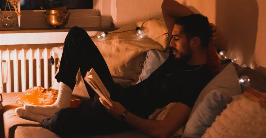 A man is reading a book while relaxing on a couch with decorative lights.