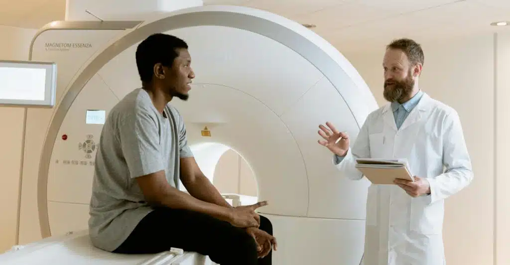 A man is sitting and talking to a doctor in a room with medical equipment.