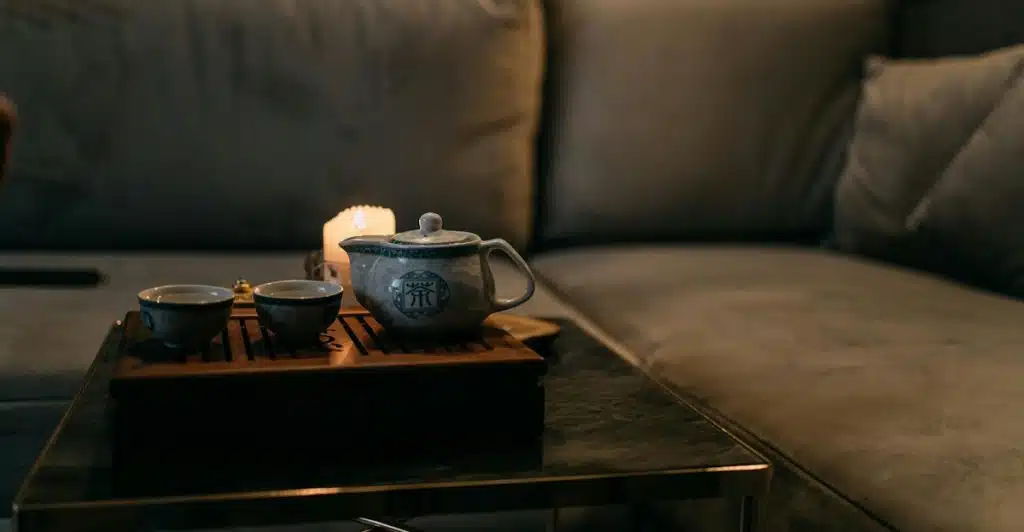A tea set is arranged on a table in a dimly lit room with a couch.