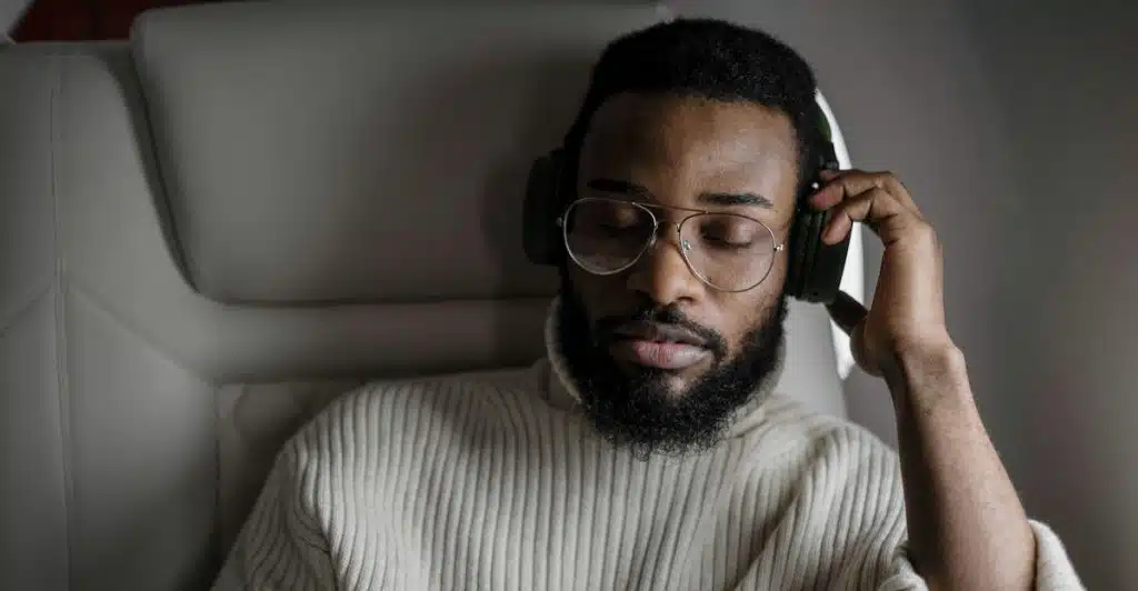 A man wearing glasses and a turtleneck sweater listening with headphones.