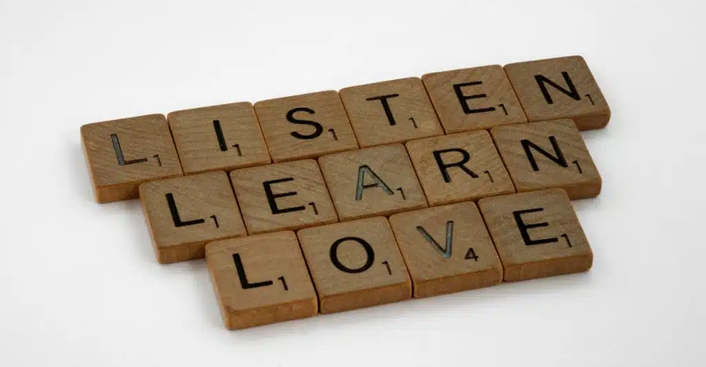Scrabble tiles arranged to spell the words "LISTEN," "LEARN," and "LOVE" on a white background.