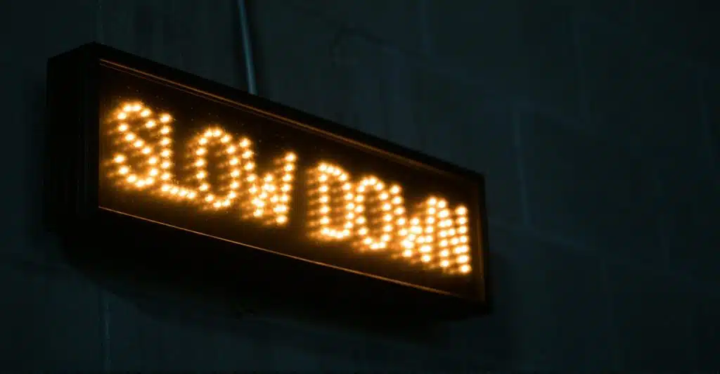 A digital sign displaying the words "SLOW DOWN" in bright orange letters against a dark, textured wall.