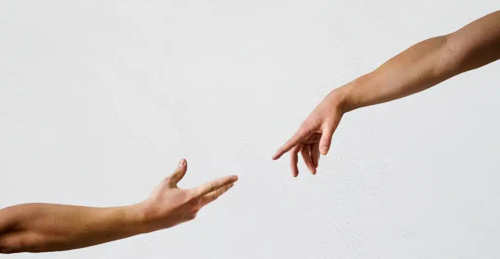 Close-up of two arms reaching towards each other with outstretched hands against a white background.