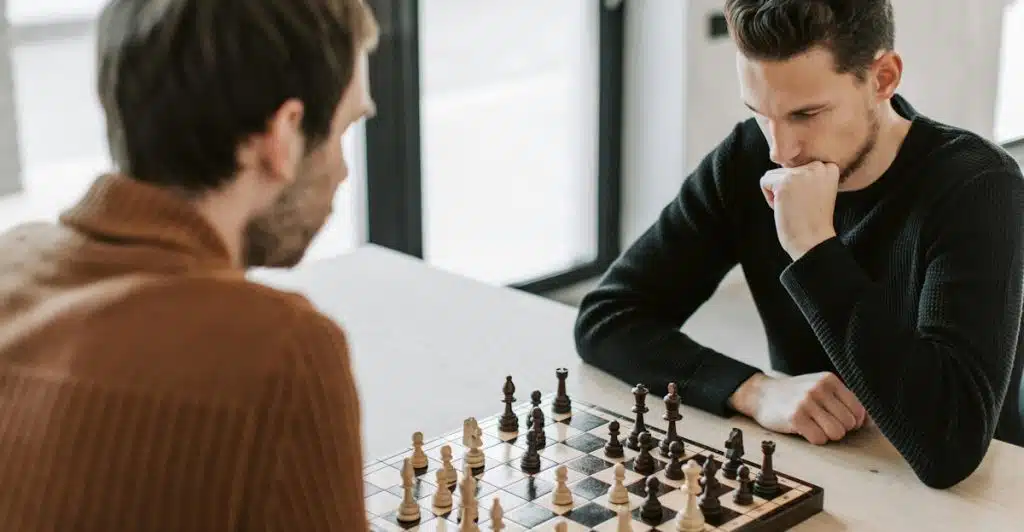 Two men intensely focused on a game of chess, sitting across from each other at a table with the chessboard between them.