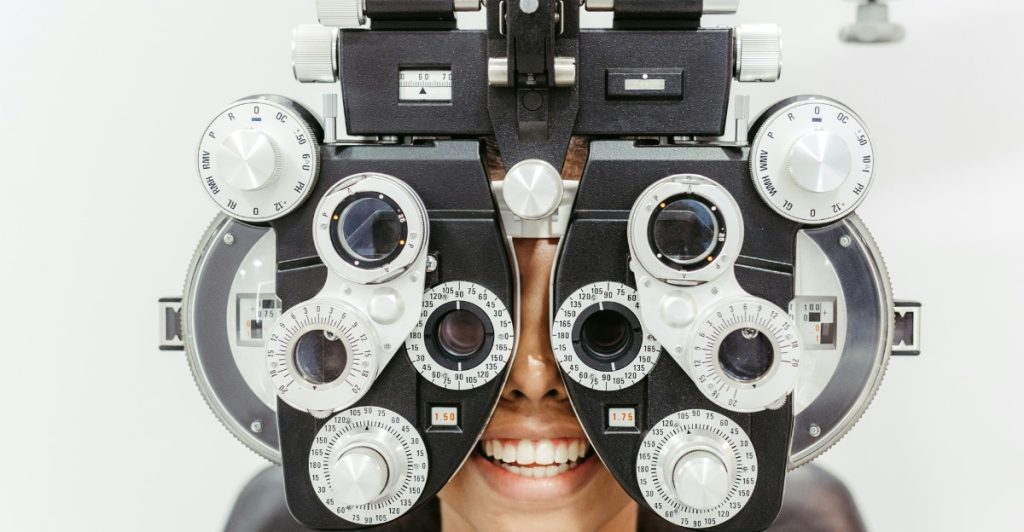 A person smiling while undergoing an eye exam with an optical instrument.