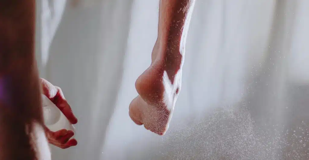 A close-up of a person's foot as white powder is sprayed onto it, with a hand visible holding the spray.