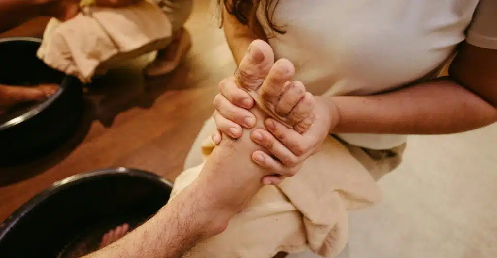 A person receiving a foot massage, with another person's hands massaging their foot over a beige cloth.