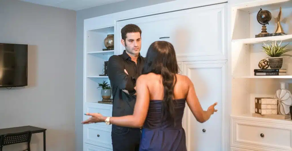 A man and a woman standing indoors, gesturing with their hands as if in a serious conversation.