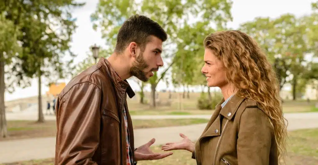 A man and a woman facing each other outdoors, gesturing with their hands in what appears to be an argument.
