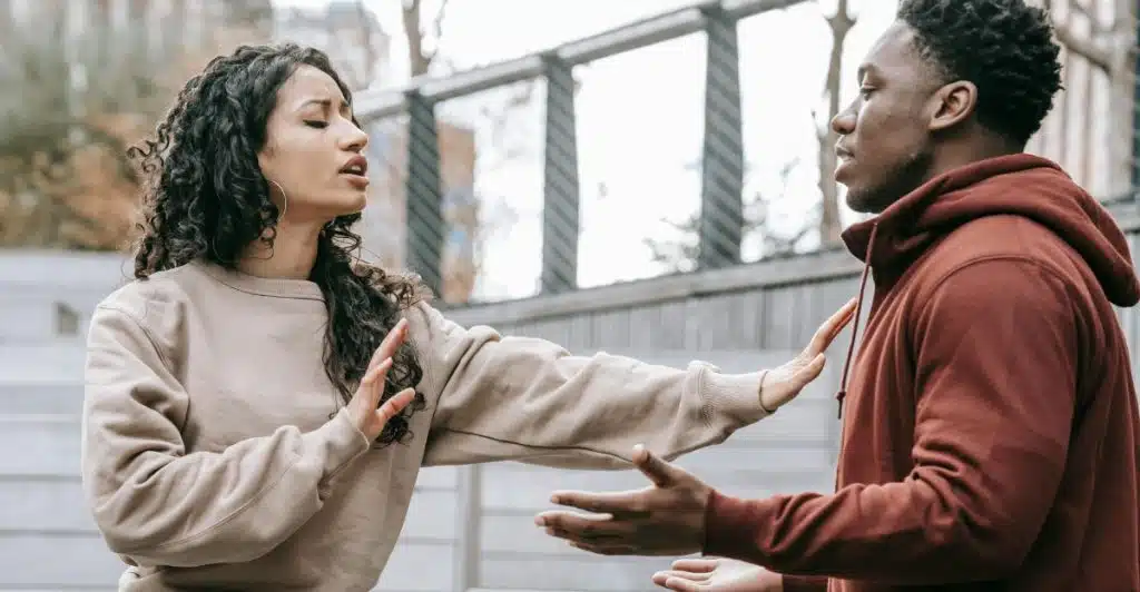 A man and a woman arguing outdoors, with the woman gesturing with her hands.