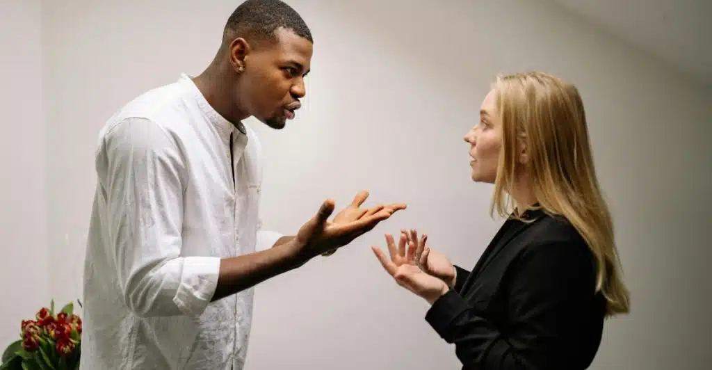 A man and a woman arguing and gesturing with their hands in an indoor setting.