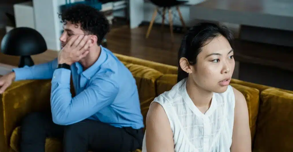 A man and a woman sitting on a couch, turned away from each other.