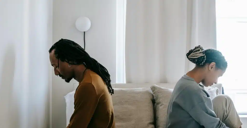 A man and a woman sitting on a bed with their backs to each other.