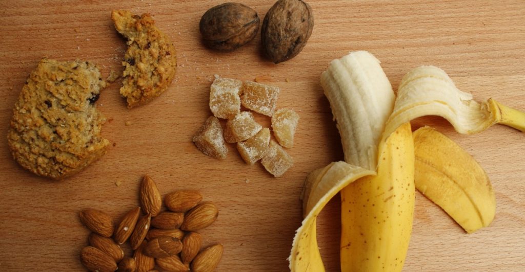 An assortment of foods including a banana, nuts, and what appears to be a baked good, illustrating complex carbohydrates.
