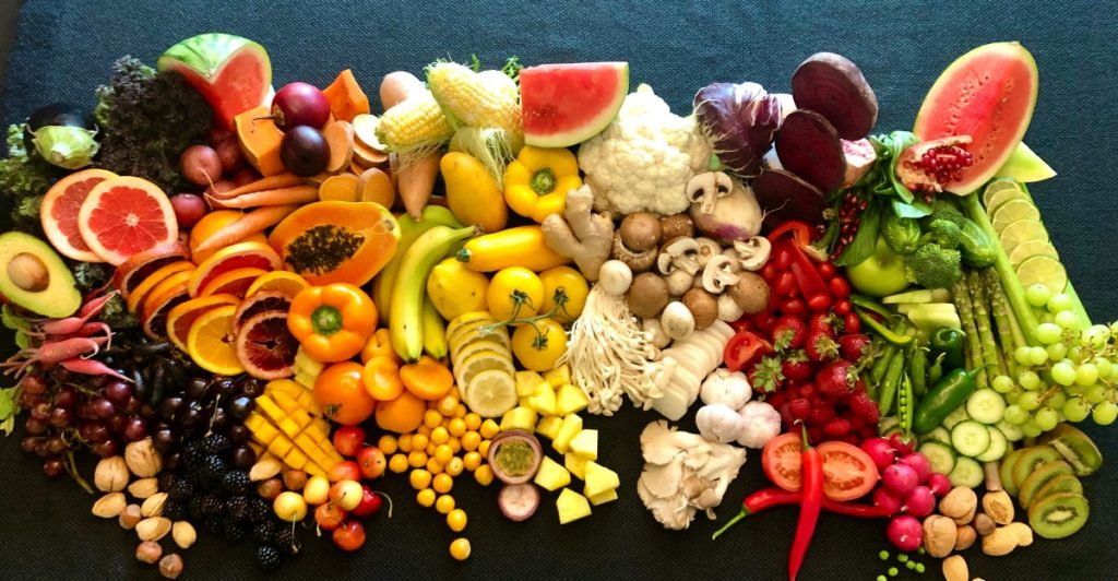 A colorful and varied selection of fruits and vegetables is arranged on a dark surface.