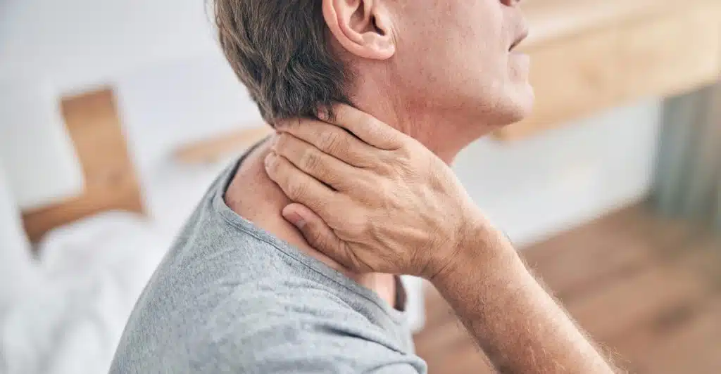A man holding the back of his neck with one hand, looking like he is experiencing pain or tension.