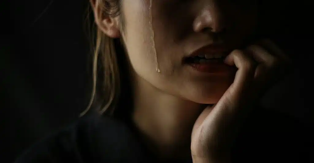 A close-up of a woman's face with tears streaming down her cheek and her hand near her mouth.