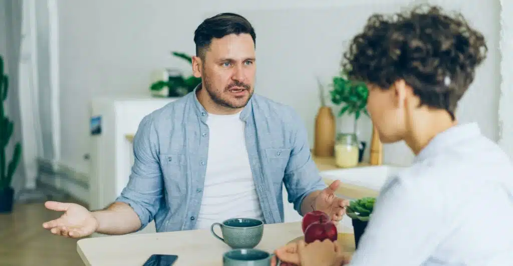 A man and a woman sitting at a table with cups, appearing to be in a serious discussion.