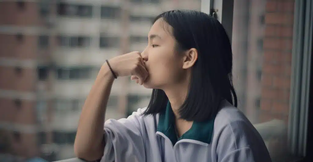 A woman looking out a window with her chin resting on her hand.