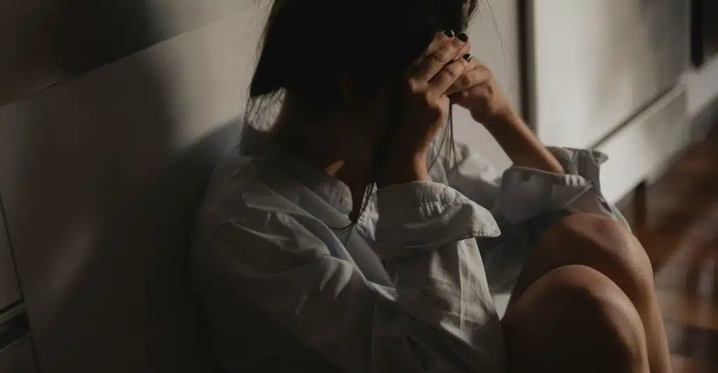 A woman sitting on the floor with her knees drawn up and her face hidden in her hands.