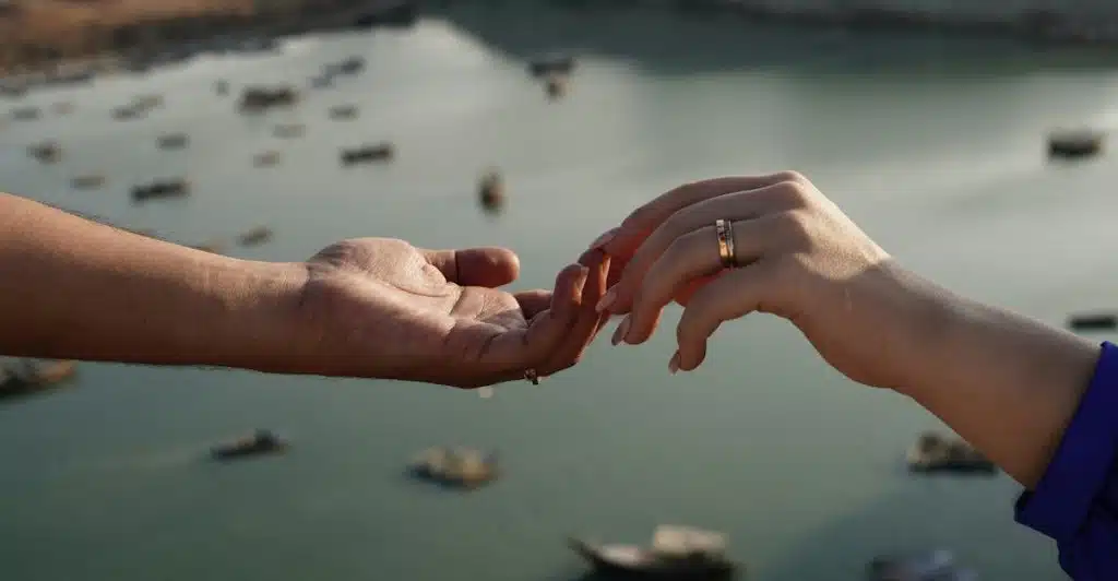Two hands, one reaching out from the left and one from the right, almost touching over water with boats.