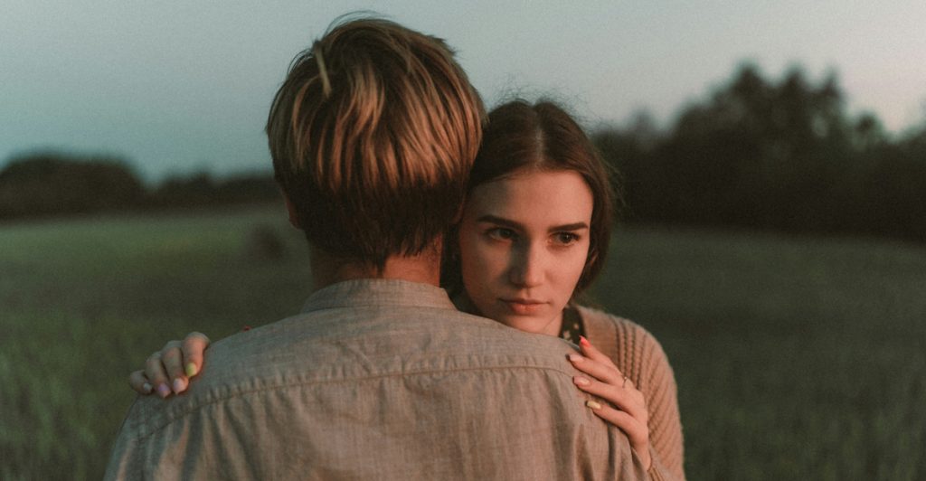 A man and a woman embracing outdoors in a lush green field.