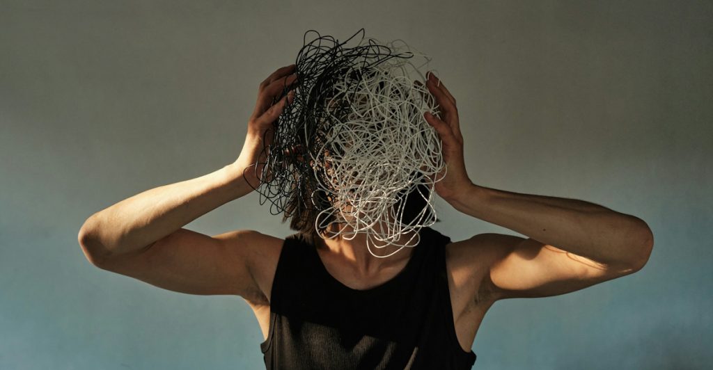 A person standing with their hands on their head, which is covered in tangled wires.