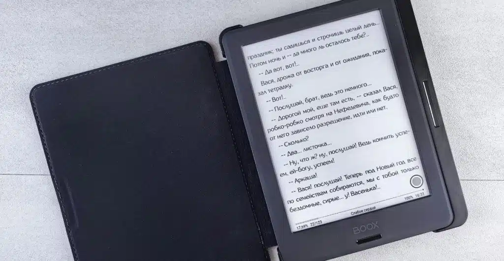 An E-Ink tablet displaying text, with its black cover open on a gray surface.