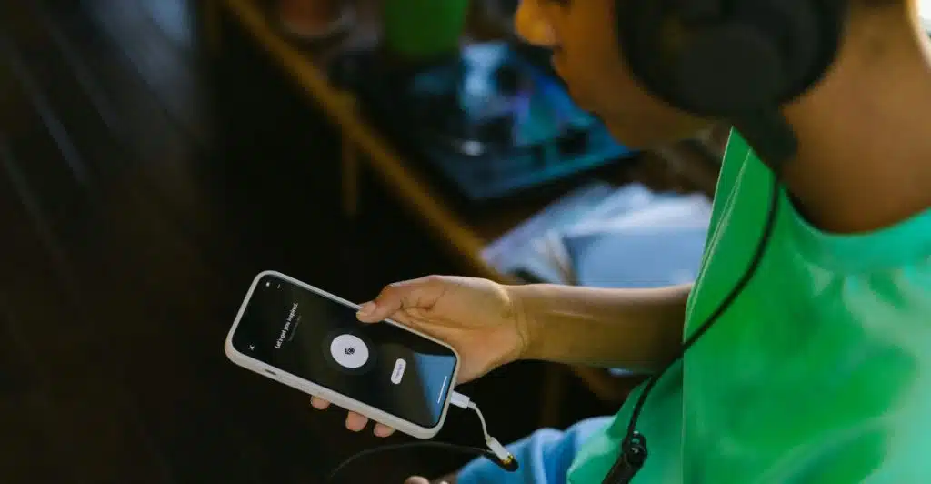 A person wearing black headphones, holding a white smartphone displaying a recording interface.