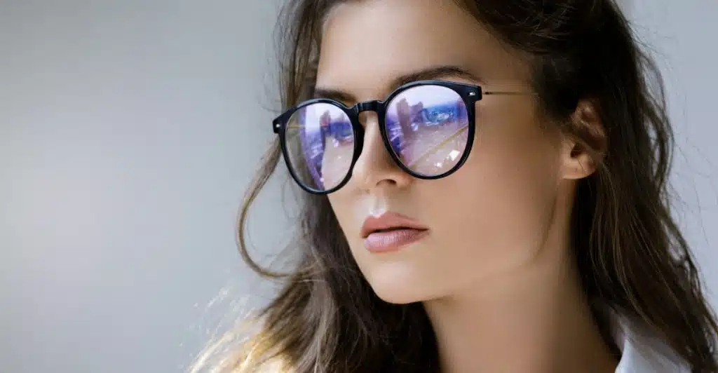 A woman with long hair wearing round, dark-rimmed blue light filtering glasses.