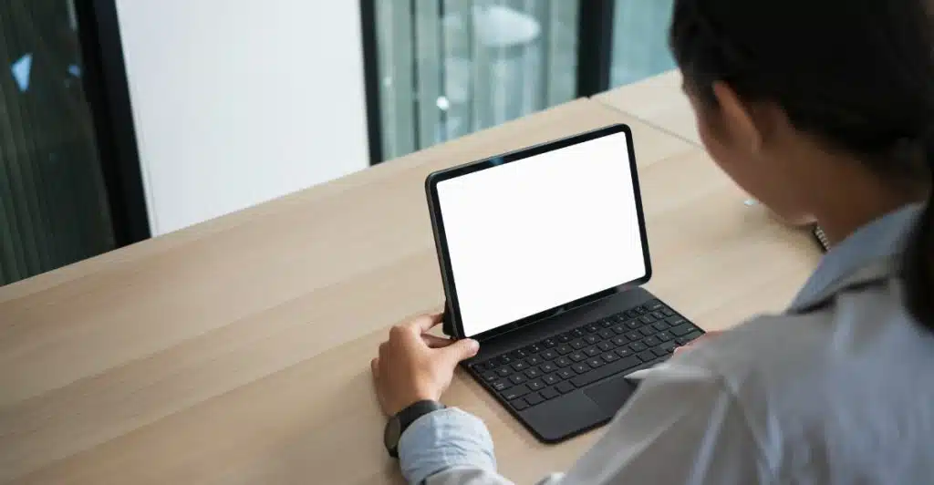 A person seen from over the shoulder, typing on a black Bluetooth keyboard attached to a tablet with a blank screen.
