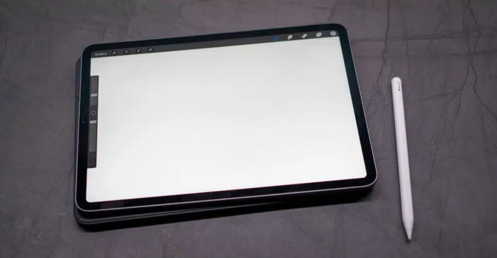 A black digital tablet with a blank white screen and a white stylus pen resting on a dark gray surface.