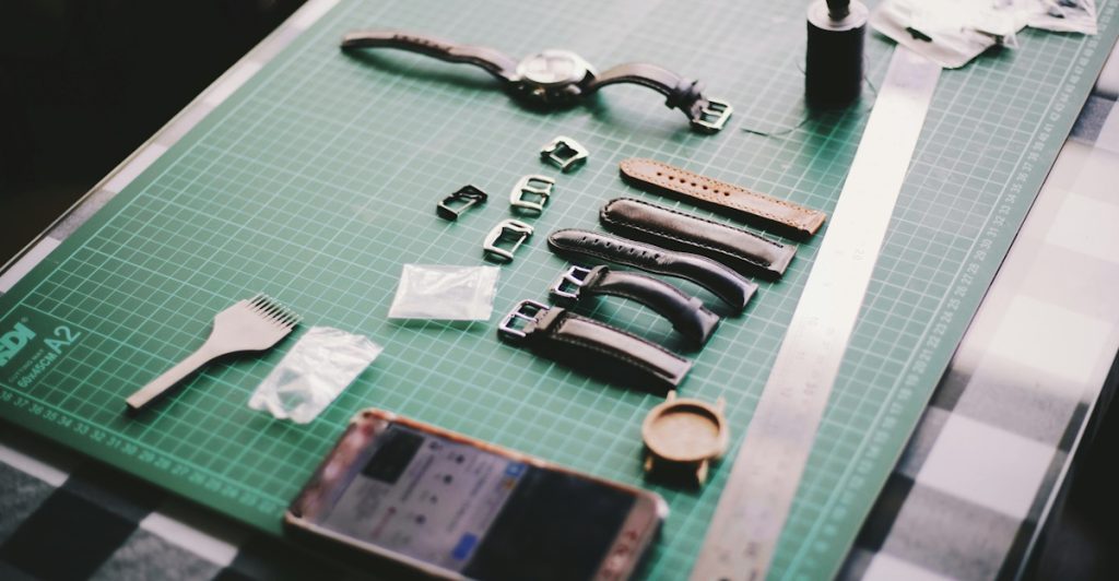 A watch, various watch straps, tools, and a smartphone laid out on a green cutting mat.