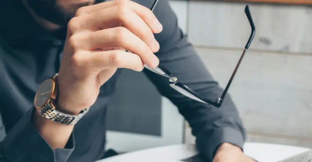 A man sitting at a table, holding a pair of glasses and looking at financial documents.