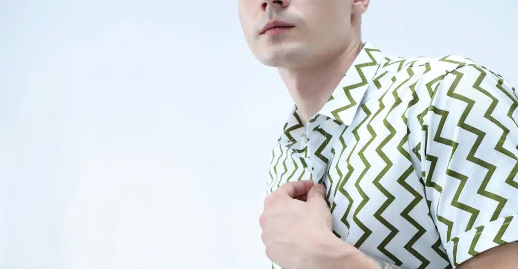 A man in a white and olive green zigzag printed short-sleeve shirt adjusting his collar.