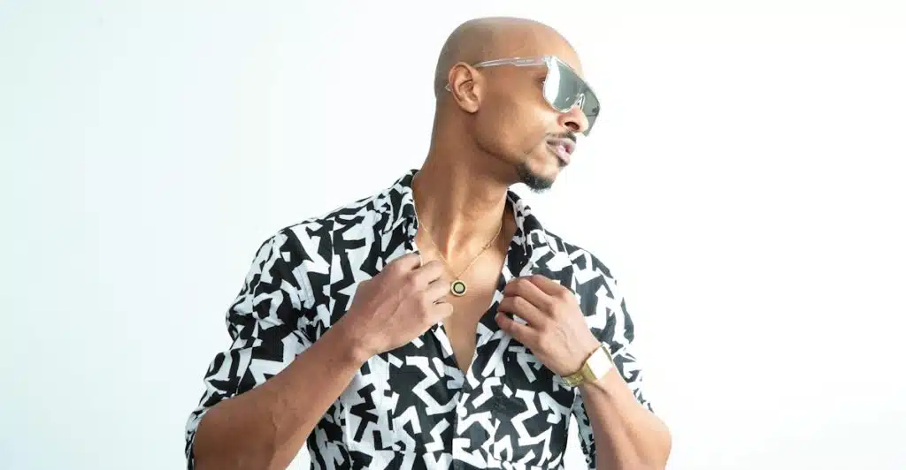 A man in a black and white abstract printed short-sleeve shirt and sunglasses looking over his shoulder.