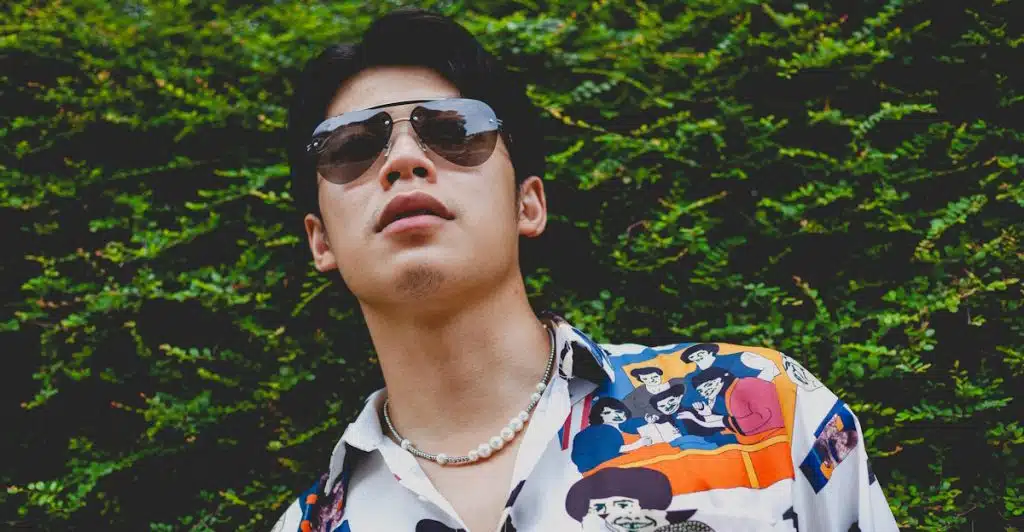 A man wearing a white shirt with cartoon character prints and sunglasses looking upwards.