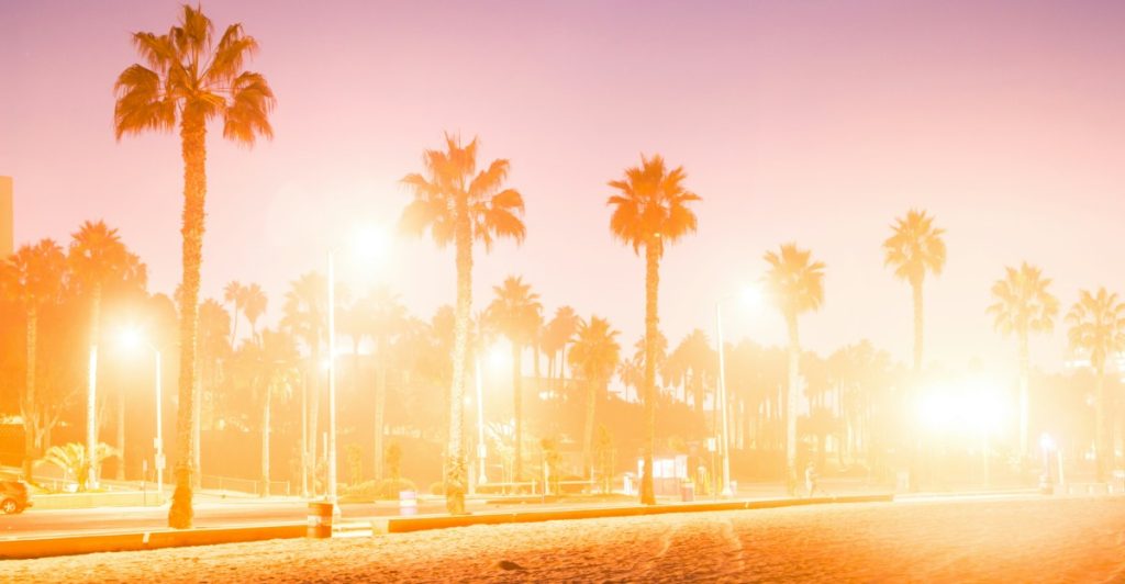 A sunset over a beach with palm trees and streetlights glowing, reminiscent of Grand Theft Auto San Andreas.