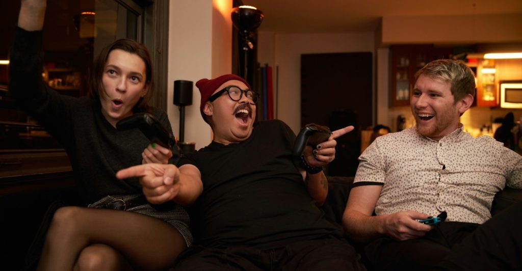 Three people enthusiastically playing video games on a couch with controllers.