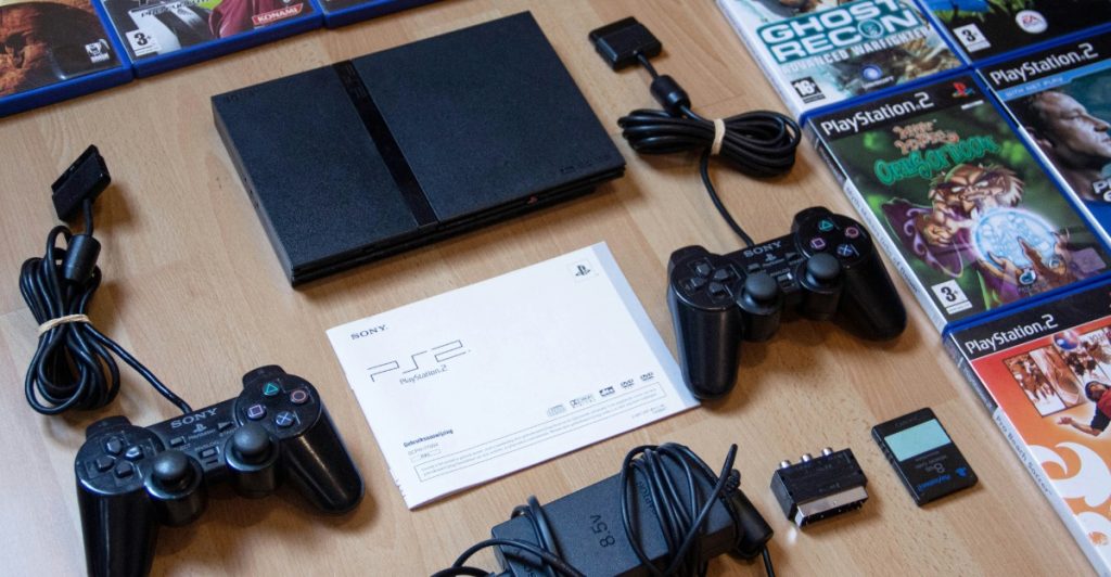 A collection of PlayStation 2 consoles, controllers, and video game cases laid out on a surface.