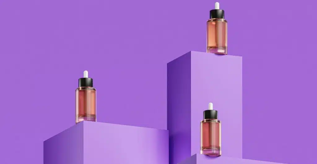 Three amber-colored dropper bottles with black tops, casting shadows, are placed on three different purple geometric platforms against a solid purple background.