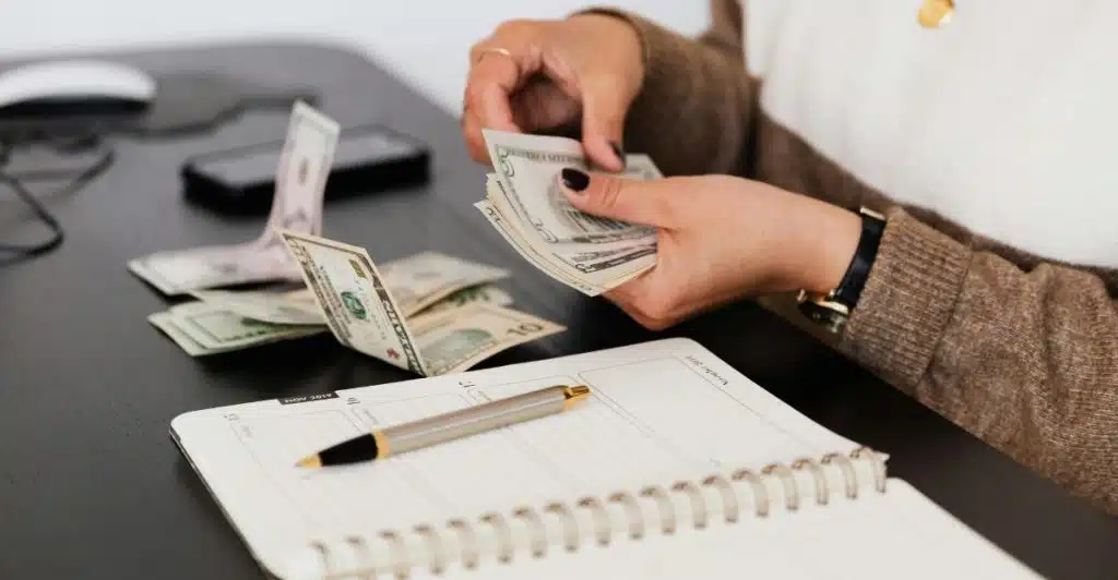 A woman's hands counting dollar bills over an open planner.