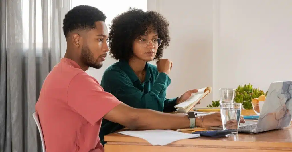A man and a woman sitting at a table, looking at a laptop.