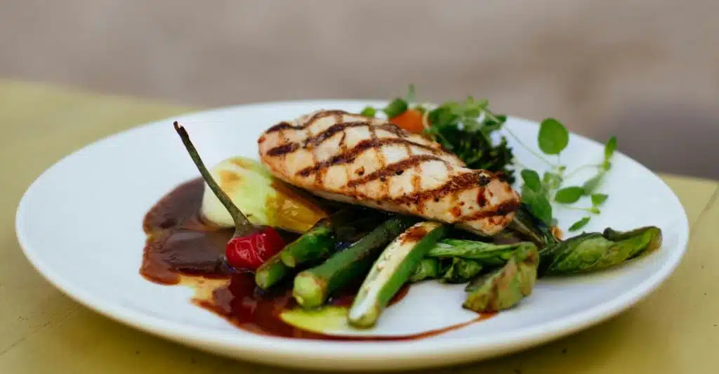 A grilled chicken breast with vegetables and a sauce on a white plate.